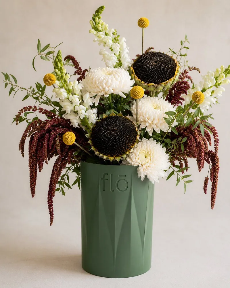 Arreglo con girasoles oscuros y flores blancas en jarrón verde de FLŌ