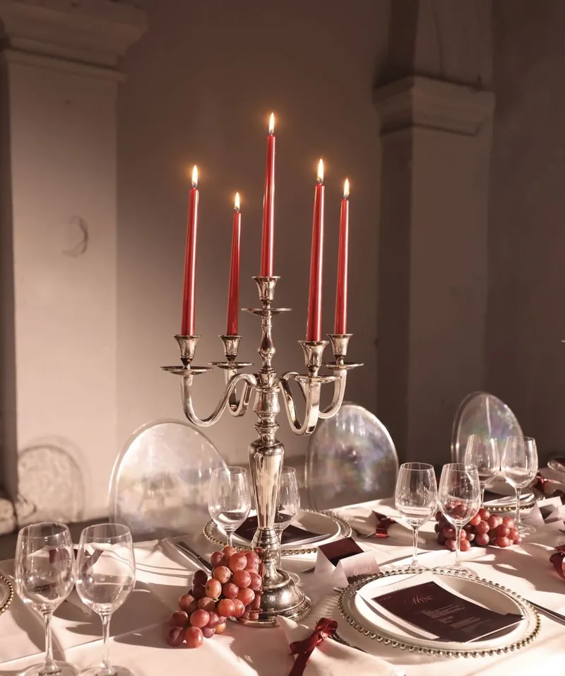 Candelabro de plata con cinco velas rojas, uvas y platos con borde dorado
