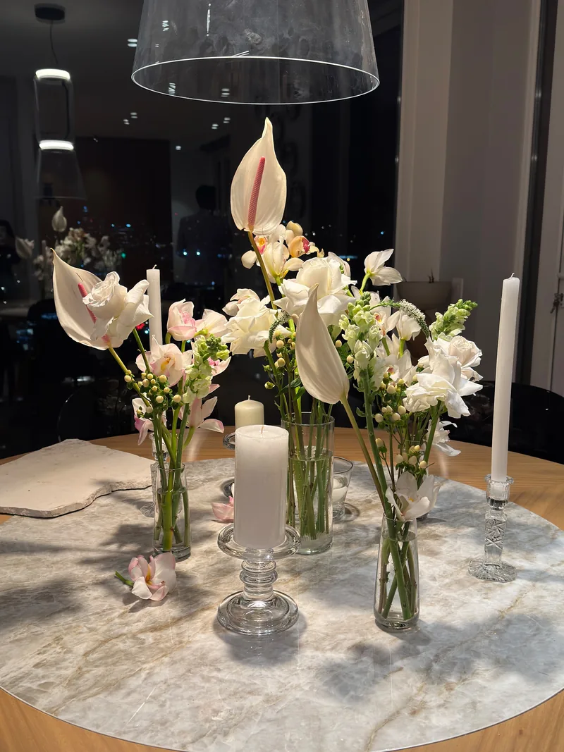 Mesa redonda de mármol con anturios, orquídeas y rosas blancas en floreros de vidrio y velas