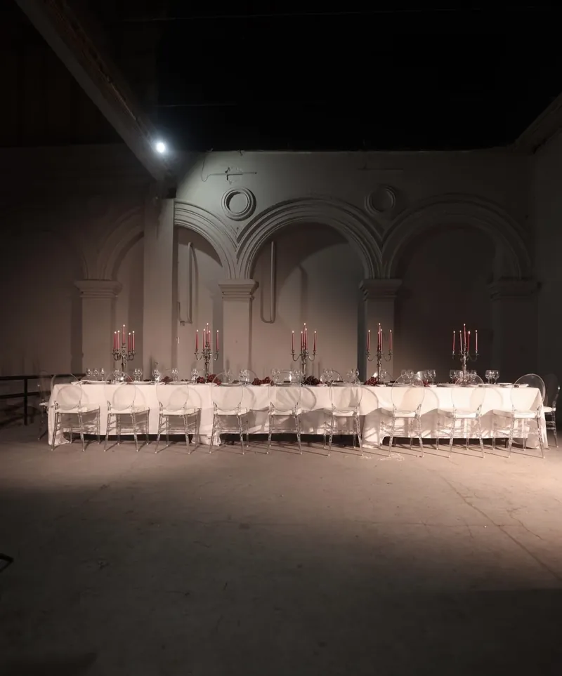 Mesa larga con mantel blanco y candelabros con velas rojas en un salón de arcos